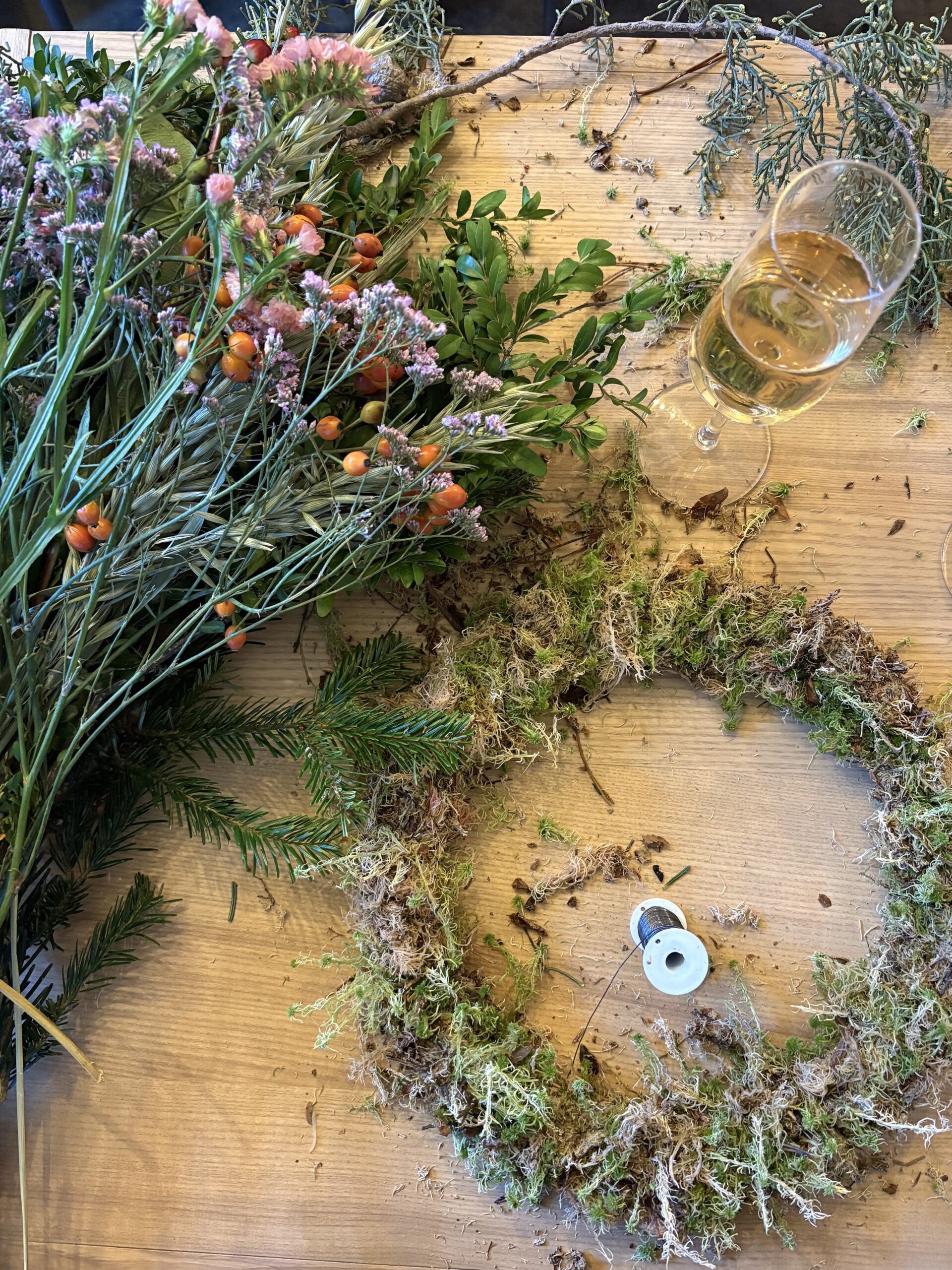 Fresh foliage, a wreath base and sparkling wine at a wreath-making workshop